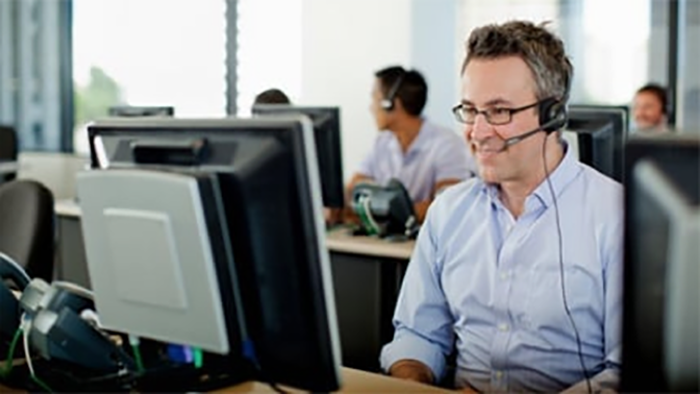 Slika tehničkog savjetnika koji gleda u monitor i preko telefona razgovara sa klijentom.